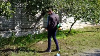 Çim biçme makinesi. Bir adam kalın bir çim biçer. Bahçe bakımı, manzara iyileştirmesi. Bahçe malzemeleri. Elektrikli çim biçme makinesi. Bitki ve yabani otların temizlenmesi. yatay resim