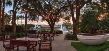 Gün batımında arka planda fıskiyelerle birlikte saklı bir bahçenin üzerinde parlayan ışıklar..