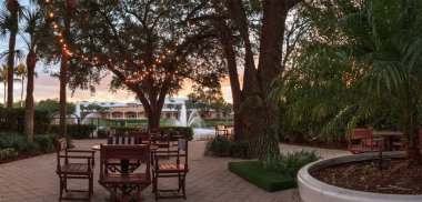 Gün batımında arka planda fıskiyelerle birlikte saklı bir bahçenin üzerinde parlayan ışıklar..