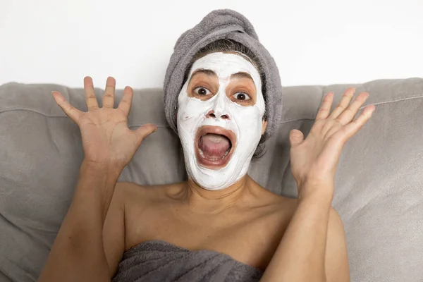 funny photo of arab woman screaming like crazy and surprised with white anti-wrinkle face mask on her face.she is wearing a towel on her head.skin care and aesthetics concept.