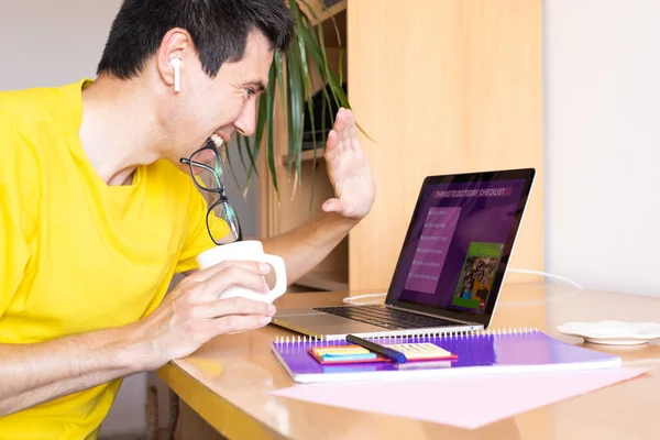 young adult man greets on a video call on his laptop while working at home