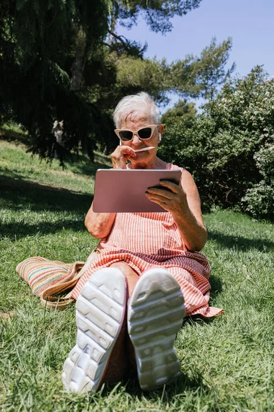 vertical image of white-haired old woman with a tablet and pencil drawing digital art. listening to music on wireless headphones