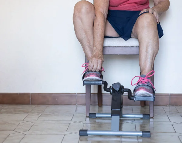 unrecognizable elderly woman exercising at home with a pedaling machine. concept of sport in elderly people and health