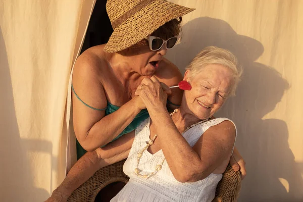 old gray-haired woman laughs as her daughter plays with her tenderly and gives her a lollipop. mother and daughter. generations of women.