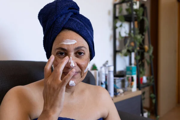 mature middle eastern woman at home applying treatment cream after a deep chemical peel with acid to remove skin blemishes.