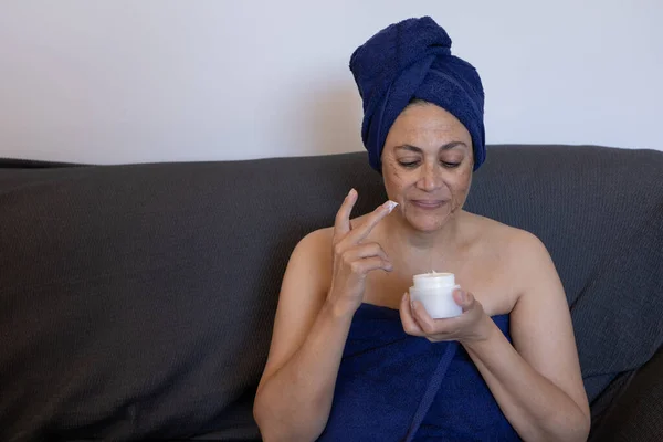 mature middle eastern woman at home applying treatment cream after a deep chemical peel with acid to remove skin blemishes.