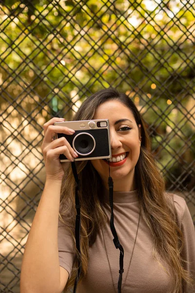 young adult latina woman smiling and taking a picture with a retro instant camera during a trip