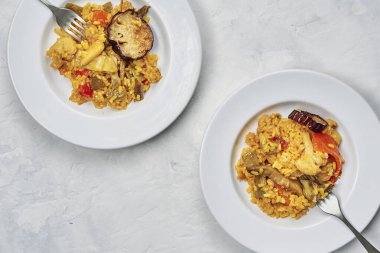 Tipik İspanyol pirinç paella 'sının beyaz masasında taze sebzelerle servis edilen iki tabak.