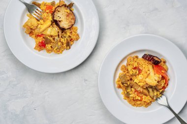 Tipik İspanyol pirinç paella 'sının beyaz masasında taze sebzelerle servis edilen iki tabak.