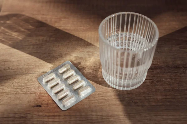 Pastillas cápsulas medicina y vaso de agua sobre fondo de madera —  Fotos de Stock