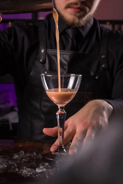 Camarero vestido con delantal negro y camisa hacen bebida de cóctel sobre fondo negro — Foto de Stock