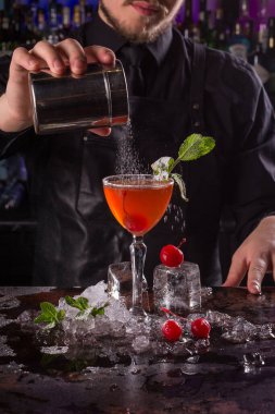 Siyah önlük ve gömlek giymiş barmen siyah arka planda turuncu kokteyl kokteyli yapar.