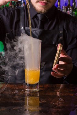 Siyah önlük ve gömlek giymiş barmen siyah arka planda kırmızı kokteyl kokteyli yapar.