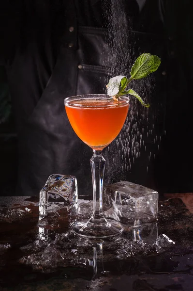 Bartender klädd i svart förkläde och skjorta gör orange cocktail dryck på svart bakgrund — Stockfoto