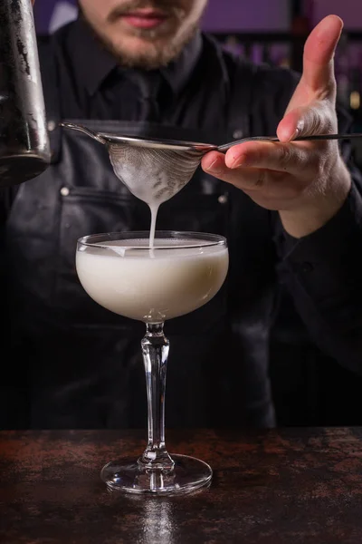 Bartender dressed in black apron and shirt make alcohol cocktail drink on black background — Stock Photo, Image