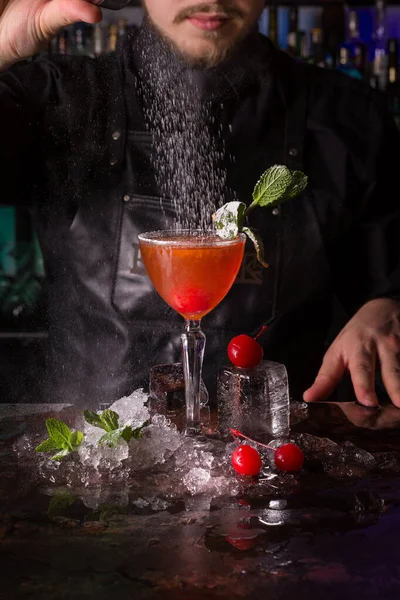 Bartender klädd i svart förkläde och skjorta gör alkohol cocktail dryck på svart bakgrund — Stockfoto
