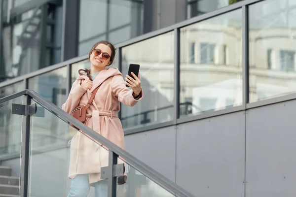 Mujer en vestido rosa tomar selfie en smarthone en gris urbano fondo al aire libre —  Fotos de Stock