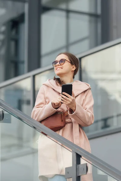 Kvinna i rosa klänning prata med smarthone utomhus på grå stad bakgrund — Stockfoto