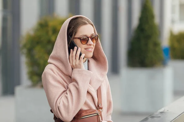 Mulher de vestido rosa falando com smarthone ao ar livre no fundo da cidade urbana cinza — Fotografia de Stock
