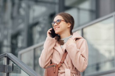 Pembe elbiseli bir kadın gri şehir arka planında zeki biriyle konuşuyor.