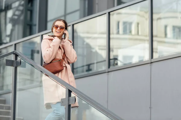 Mujer en vestido rosa hablando con smarthone al aire libre sobre fondo gris urbano de la ciudad —  Fotos de Stock