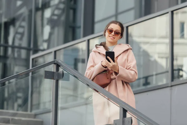 Mujer en vestido rosa hablando con smarthone en fondo urbano gris al aire libre —  Fotos de Stock