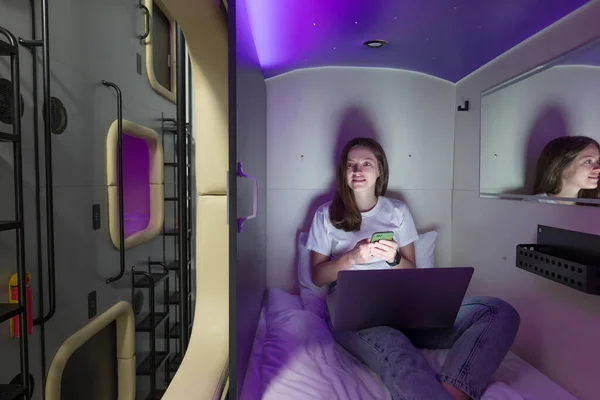 Woman in capsule space hotel sitting with gadget