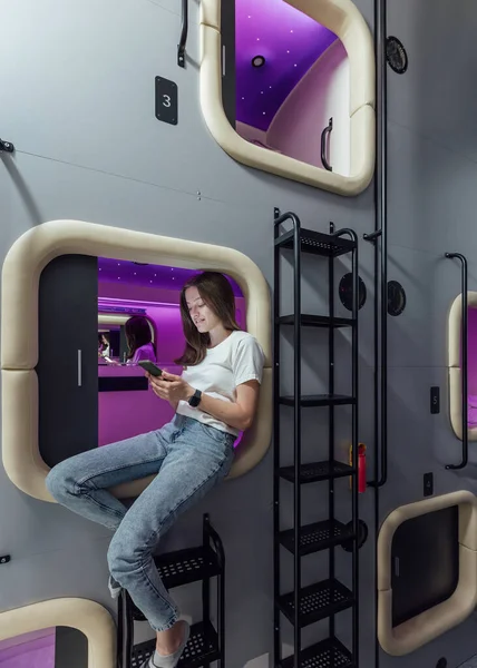 Woman in capsule space hotel sitting with gadget