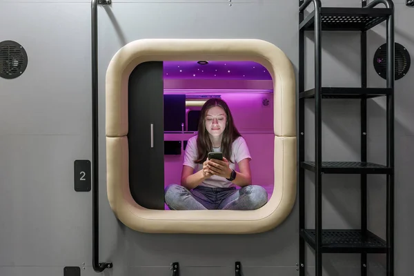 Woman in capsule space hotel sitting with gadget