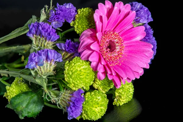 Güzel bir pembe, yeşil ve mor kesim çiçekleri siyah bir yüzey üzerinde uzanır..