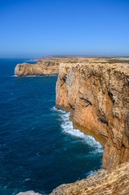 Portekiz 'deki Algarve' de yüksek engebeli kayalıkları olan güçlü dalgaları olan bir sahil..
