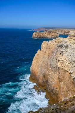 Portekiz 'deki Algarve' de yüksek engebeli kayalıkları olan güçlü dalgaları olan bir sahil..