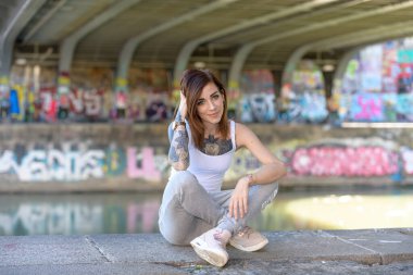 Güzel, genç ve dövmeli bir kadın nehrin kenarında oturuyor ve sıcak yazın tadını çıkarıyor..