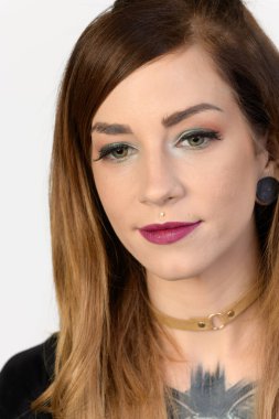 Yakından çekilen portre, beyaz arka planda tasması olan oldukça genç ve makyajlı bir kadın..