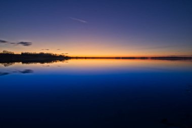 Büyük bir gölde gün batımından sonra mavi saatte, harika bir portakaldan mavi renkli gökyüzüne.