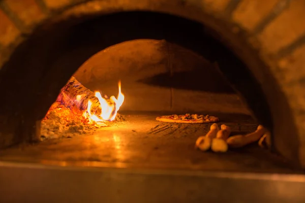 A pizza and pizza bread is baked in a pizza oven fired with glowing and burning wood.