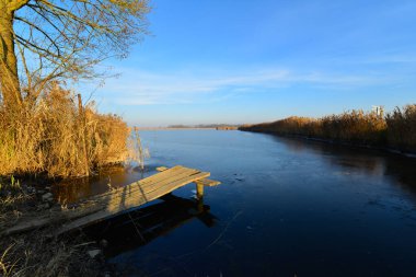 Sonbaharın sonlarında soğuk güneşli bir günde küçük bir iskelesi olan büyük bir balık havuzu..