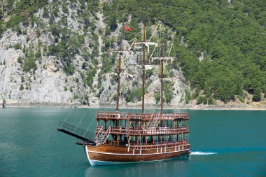 Oymapinar barajı yakınlarındaki dağ kayalıkları arasında üç direkli bir turist yatı yüzüyor. Yeşil Kanyon, Manavgat, Antalya, Türkiye