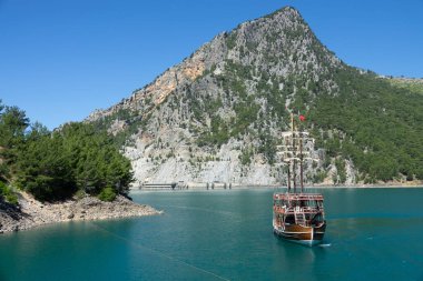 Oymapinar barajı yakınlarındaki dağ kayalıkları arasında üç direkli bir turist yatı yüzüyor. Yeşil Kanyon, Manavgat, Antalya, Türkiye