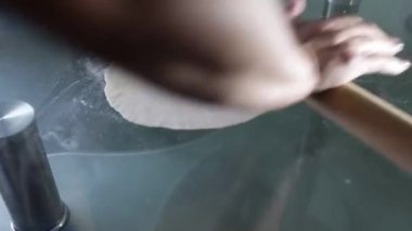 Bir kadın masanın üzerinde merdaneyle hamuru yuvarlıyor.