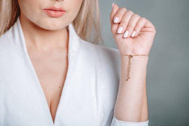 Beyaz ceketli bir bayanın bileğinde altın bilezik var..