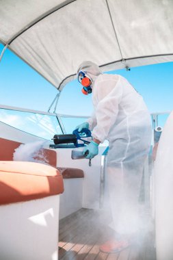Özel üniformalı bir adam tekneyi dezenfekte eder..