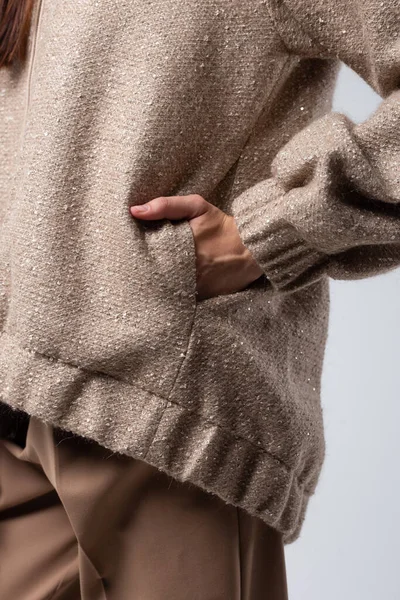 Beyaz bir arka planda, kapüşonlu bir kazağın cebindeki bir kadının yakın plan fotoğrafı.