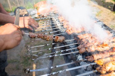 Erkeklerin elleri yakın planda ızgarada barbekü pişiriyor. Sokaklarda pişen et dumanı.