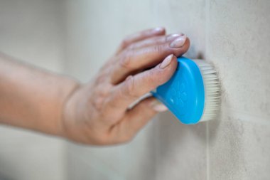 Bir adamın eli, mavi bir fırçayla fayans duvarını temizler..