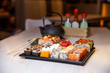 rolls on a black square plate and a teapot of tea.