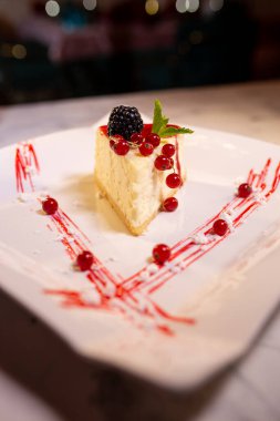 Böğürtlenli beyaz tabakta taze New York peynirli keki. Bir yemek restoranında tatlı servisi..