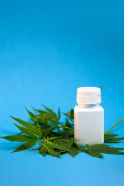 Mavi arka planda bir dal esrar bulunan beyaz bir ilaç kavanozu..