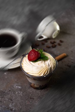 Classic tiramisu dessert with strawberries in a cup and coffee on the table.