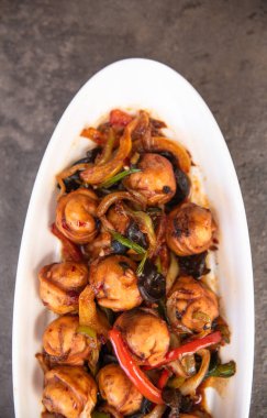 Beton bir zeminde beyaz bir tabakta kızarmış hamur köftesi.